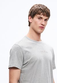 Hall halli puuvillaseguga t-särk ümara kaelusega, millel on rinnal peen tikitud logo. Lühikesed keha järgivad varrukad ja klassikaline lõige.