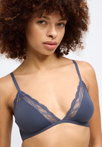 Soutien-gorge sans fil bleu foncé avec des bordures en dentelle. Tissu lisse avec un délicat surcroît de dentelle florale. Design à cups triangulaires.