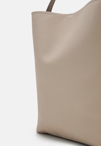 Gros plan d'un sac à main en cuir beige texturé avec une seule bandoulière sur un fond clair.