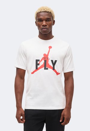 Jeune homme aux cheveux blonds courts porte un t-shirt blanc avec une silhouette rouge d’un joueur de basket sautant et le mot « FLY » en lettres noires en gras.