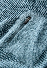Helles blaues Strickpullover mit einem strukturierten Design, einer Reißverschlusstasche vorne mit einem schwarzen YKK-Reißverschluss und einem gerippten Kragen.