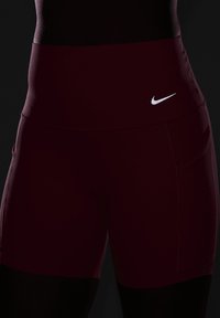 Burgundi värvi spordilühikesed püksid kõrge vöökoha ja küljetaskutega. Esiküljel on väike valge Nike logo. Sile ja elastne kangas.
