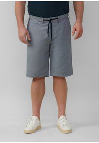 Herren Shorts in knielanger Länge aus karierter grauer Stoff, mit einem Kordelzugbund und seitlichen Taschen, kombiniert mit weißen Sneakers.