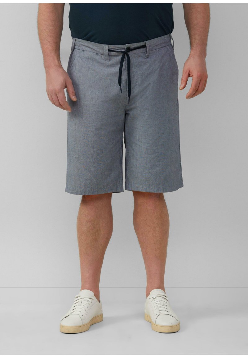 Herren Shorts in knielanger Länge aus karierter grauer Stoff, mit einem Kordelzugbund und seitlichen Taschen, kombiniert mit weißen Sneakers.