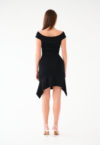 Czarna, dopasowana sukienka z dekoltem bez ramiączek, marszczonym biustem, asymetrycznymdołem i gładką teksturą, w zestawieniu z cielistymi sandałami na wysokim obcasie.