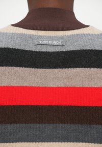 Nærbilde av en flerfarget stripete strikkegenser med brun krage og en "TORY BURCH" stoffetikett på øvre bak.