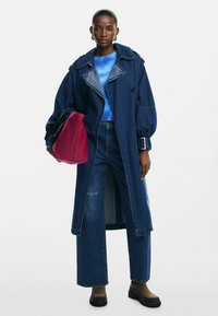 Denim plašč s čezmernimi rokavi in pasom, v kombinaciji z modrim pletenim topom in hlačami z visokim pasom. Nosila maroon torbico; sproščen kroj.