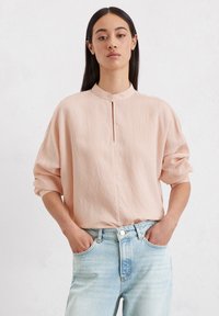 Hellbeige übergroße Bluse mit vertikalen Streifen, Stehkragen und Knopfleiste. Kombiniert mit hellblauen Jeans.