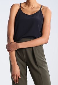 Ciemnoniebieski top bez rękawów z cienkimi ramiączkami, wykonany z gładkiego materiału. Noszony z wysokim stanem oliwkowymi spodniami z zakładkami.