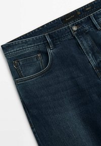 Tummansiniset farkut, joissa on sileä pinta. Mukana etutasku, vyölenkit ja napitettavuus vyötäröllä. Ei näkyvää kulutusta.