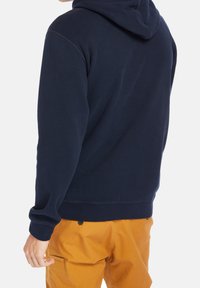 Navyblauwe hoodie met een zachte textuur, voorzien van een kangoeroezak en geribbelde manchetten, gecombineerd met beige broek.