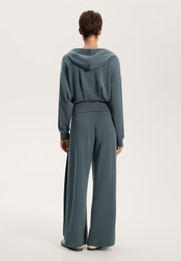 Felpa blu chiaro con cappuccio, dal taglio rilassato, abbinata a pantaloni a gamba larga in tessuto coordinato. Texture liscia ed elementi di design casual.