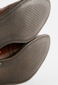 Chaussures en cuir marron avec une semelle en caoutchouc texturé, ornée d'un motif tissé et de perforations décoratives sur les bords.