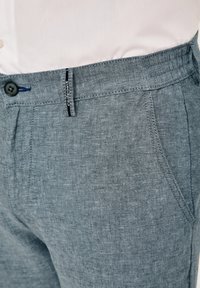 Gray linen pants featuring an elastic waistband, button closure, side pockets, and a subtle texture with a branded tag on the front.