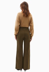 Jasnobrązowy sweter z dzianiny w oversize'owym kroju oraz oliwkowe szerokie spodnie z wysokim stanem, o gładkiej fakturze i subtelnych detalach przeszyć.