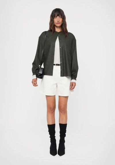 Oliven grønn skjorte med knapper, hvit t-skjorte, hvite shorts, svart belte, svart håndveske, svarte knesokker, spisse svarte hæler.