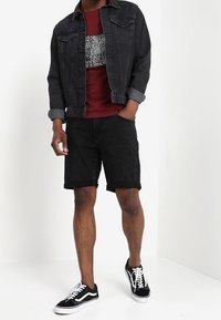 Chaqueta de mezclilla negra con puños azul claro, camiseta burdeos con un diseño gráfico negro, pantalones cortos negros y zapatillas negras y blancas.