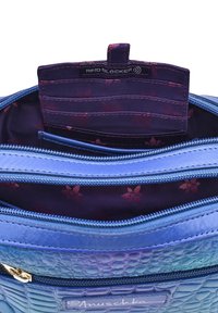 Blauwe tas met textuur, met open ritscompartimenten die een paars bloemeninterieur en RFID-blokkerende kaartsleuven tonen.