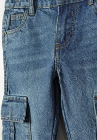 Pantalones cargo de mezclilla azul con múltiples bolsillos, costuras visibles y una superficie texturizada. El diseño incluye un corte recto y una cinturilla clásica.