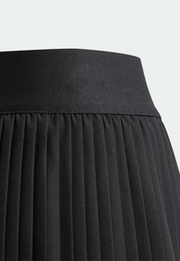 Falda negra plisada con una amplia cinturilla elástica; presenta una textura vertical y pliegues uniformes para un aspecto estructurado.