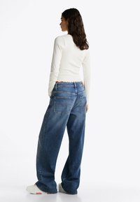 Jeans in denim blu dal taglio ampio, a vita alta, con tasche posteriori e dettagli di cucitura discreti, abbinati a un top bianco attillato.