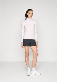Lys rosa zip-up sportsjakke med lange ærmer, parret med sorte shorts. Hvide sneakers fuldender outfittet. Simpelt, funktionelt design.