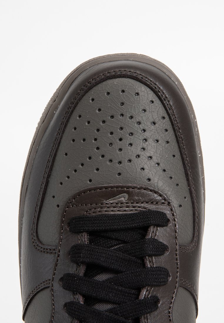 Zapatilla negra con parte superior de cuero texturizado, que presenta perforaciones para la transpirabilidad y un sistema de cierre con cordones negros. Diseño de punta redonda.