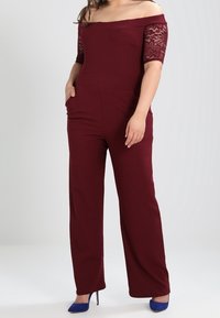 Bordeauxroter Jumpsuit mit schulterfreiem Design und Spitzensäumen, ausgestattet mit Fronttaschen und geradem Bein.