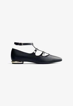 Chaussure plate pointue en cuir noir avec bride de cheville, boucle dorée, perles décoratives en perle et petit talon rehaussé de doré.