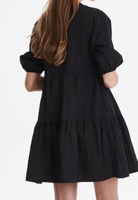 Robe en coton noir avec un design à volants, des manches bouffantes et une coupe décontractée, présentant une texture unie et une longueur au genou.