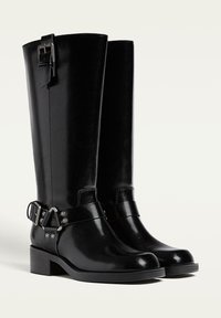 Schwarze Lederstiefel in Kniehöhe mit eckiger Zehenform und Blockabsatz, ausgestattet mit einer seitlichen Schnalle und Riemendetails. Glatte Textur mit hochglänzender Oberflächenbehandlung.