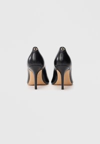 Chaussures à talons hauts en cuir noir avec un bout pointu et un talon aiguille. Présentent un accent logo doré à l'arrière. Texture lisse.