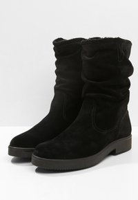 Černé semišové boty s volným střihem, které mají měkkou vnitřní podšívku, plochou gumovou podrážku a prošití po stranách pro přidané detaily a texturu.