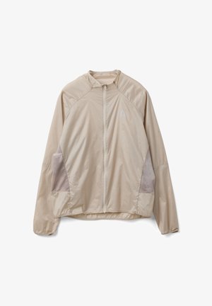 Beige leichte Jacke mit langen Ärmeln, Frontreißverschluss, hohem Kragen und dunkleren beigen Seitenpaneelen zur Belüftung oder als Stilmerkmal.