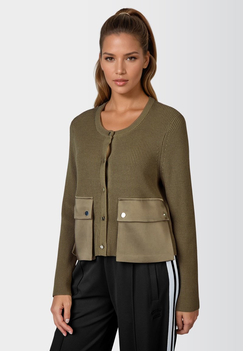 Olivgrüner Cardigan mit geripptem Textur, Knopfschluss und zwei Fronttaschen. Mit einem kontrastierenden, wildlederähnlichen Stoff am unteren Ende gestaltet.