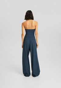 Marinblå, axelbandslös jumpsuit med vida byxben. Slät, strukturerad tyg med sömmar och fickor för extra detalj.