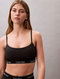 Black bralette with thin straps, featuring a Calvin Klein logo band. Smooth fabric with a minimalist design and no additional patterns.