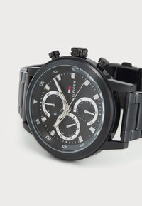 Montre chronographe noire avec un bracelet en acier inoxydable noir texturé, un élégant cadran rond et trois sous-cadrans. Marqueurs d'heure et aiguilles en argent.