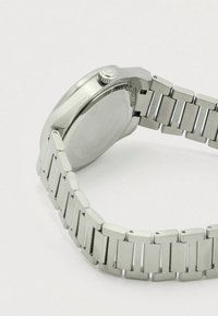 Nerūdijančio plieno laikrodis su apvaliu korpusu ir blizgiu sidabro spalvos dirželiu. Ant nugarėlės yra tekstūruotas raštas ir vainikėlis laikrodžio nustatymams.