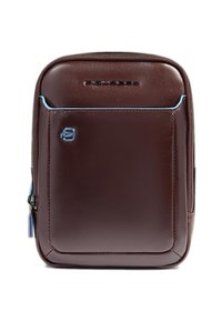 Mochila de cuero marrón con textura suave, detalles en azul contrastante, bolsillo frontal con cremallera y detalle de logo. Forma rectangular compacta.