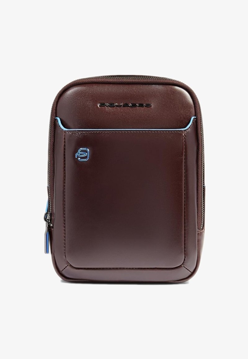 Mochila de cuero marrón con textura suave, detalles en azul contrastante, bolsillo frontal con cremallera y detalle de logo. Forma rectangular compacta.