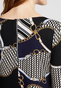 Mångfärgad klänning med geometriska mönster, kedjemönster och dragkedja på baksidan. Materialen inkluderar tyg med en texturerad yta.