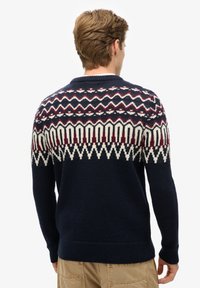 Strickpullover in Marineblau mit gemustertem, strukturiertem Schulterbereich in Creme, Burgunderrot und dunkelroten Zickzack- und geometrischen Designs. Gerippte Bündchen und Saum.
