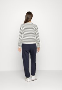 Pasiasty, długi rękaw w kolorze kremowym i granatowym, w połączeniu z granatowymi spodniami dresowymi. Koszulka ma okrągły dekolt i elastyczne mankiety.