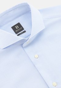 Hellblaues, schmal geschnittenes Hemd mit strukturiertem Muster, Knopfleiste vorne und sichtbarem schwarzem Markenetikett im Kragen.