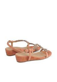 Suede sandals in soft coral with a low wedge heel, featuring an embellished strap and an adjustable ankle buckle for fit.