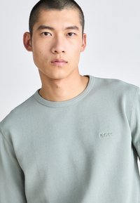 Lichtgroene geribbelde sweatshirt met een ronde halslijn. Heeft subtiele "BOSS" logo in bijpassende borduur op de borst. Zachte textuur.