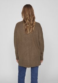 Ruskea neulottu ylipitkä neuletakki, jossa on tekstuuri, pitkät hihat ja korkea-alareunat. Yhdistetty sinisiin farkkuihin.