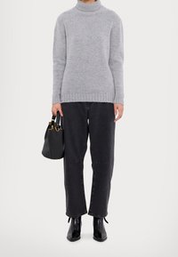 Pull à col roulé gris clair en maille, pantalon en denim noir ample, bottines et petit sac à main noir avec un accent doré.