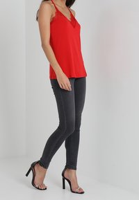 Rode satijnen camisol met kanten afwerking, gecombineerd met donkergrijze skinny jeans en zwarte stilettohakken met heldere edelsteenaccenten.